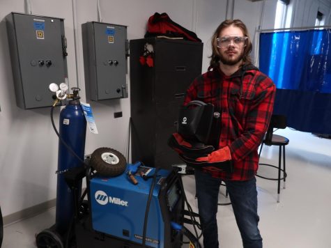 Linkel holding a face shield next to a welding cart.